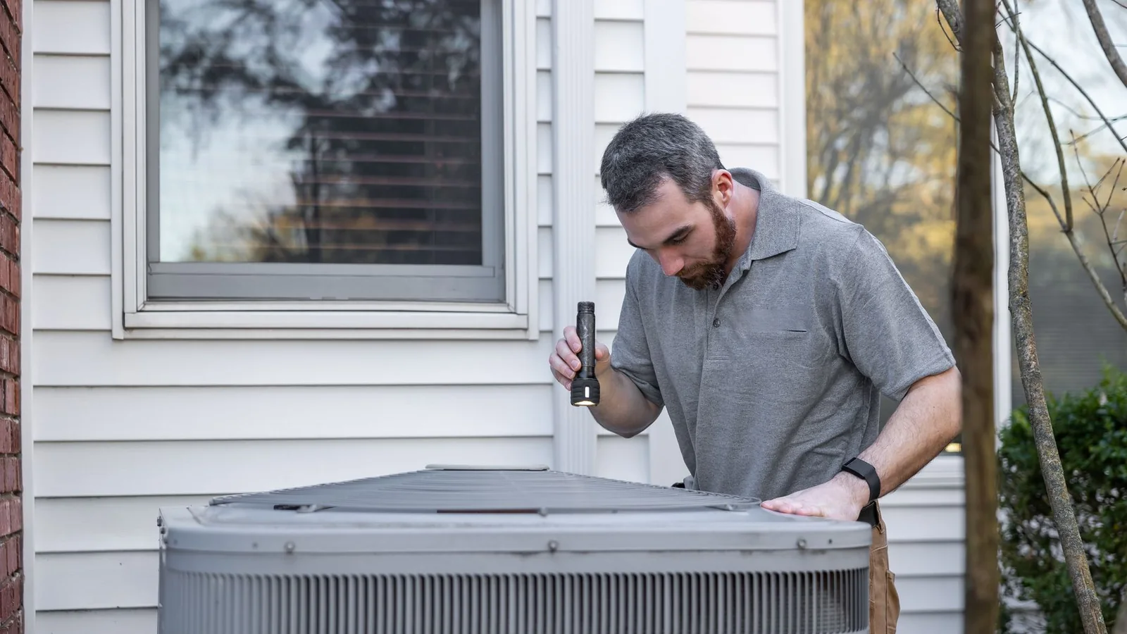 Technician inspecting a residential outdoor HVAC unit with a flashlight